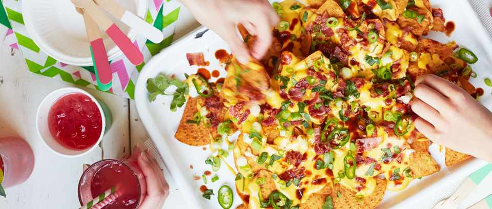 Bacon loaded nachos on a platter with a hand taking a piece