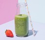 A strawberry and avocado smoothie in a glass bottle with a paper straw