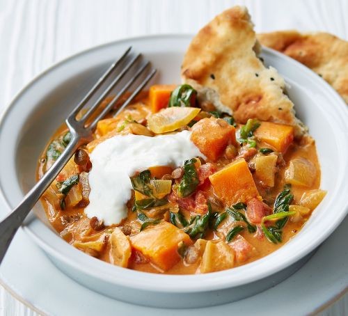 Squash and spinach curry with naan bread in a bowl