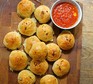Cheese-stuffed garlic dough balls on a wooden board with a tomato sauce dip alongside
