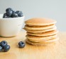 Stack of healthy American pancakes on table with blueberries in bowl