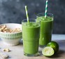 Green smoothie in glasses with straws, alongside sliced limes and nuts