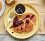 Three lemon and ricotta pancakes served on a plate with blueberry maple syrup
