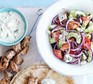 Greek salad in a bowl alongside kebabs and tzatziki