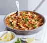 Paella in a large pan with serving spoon and lemon wedges